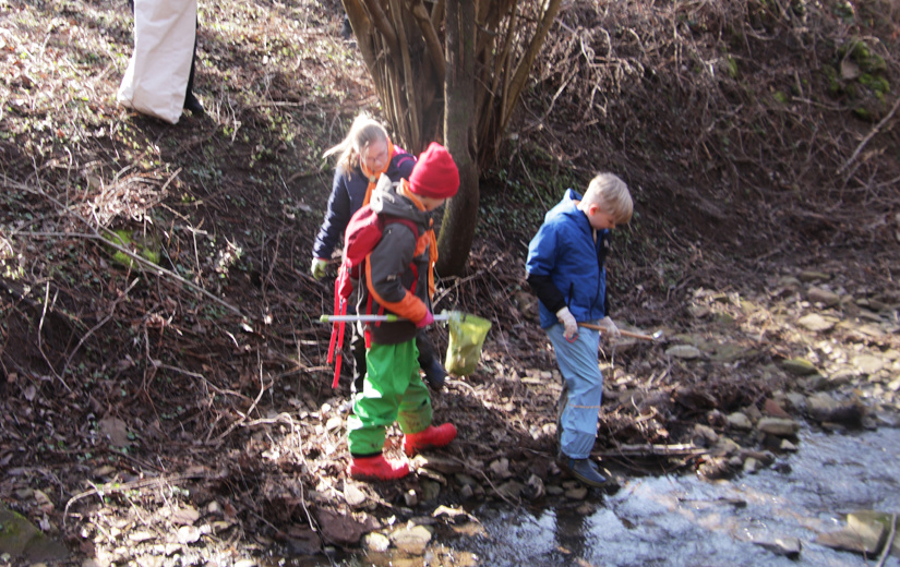 Kinder säubern den Bachlauf von Müll